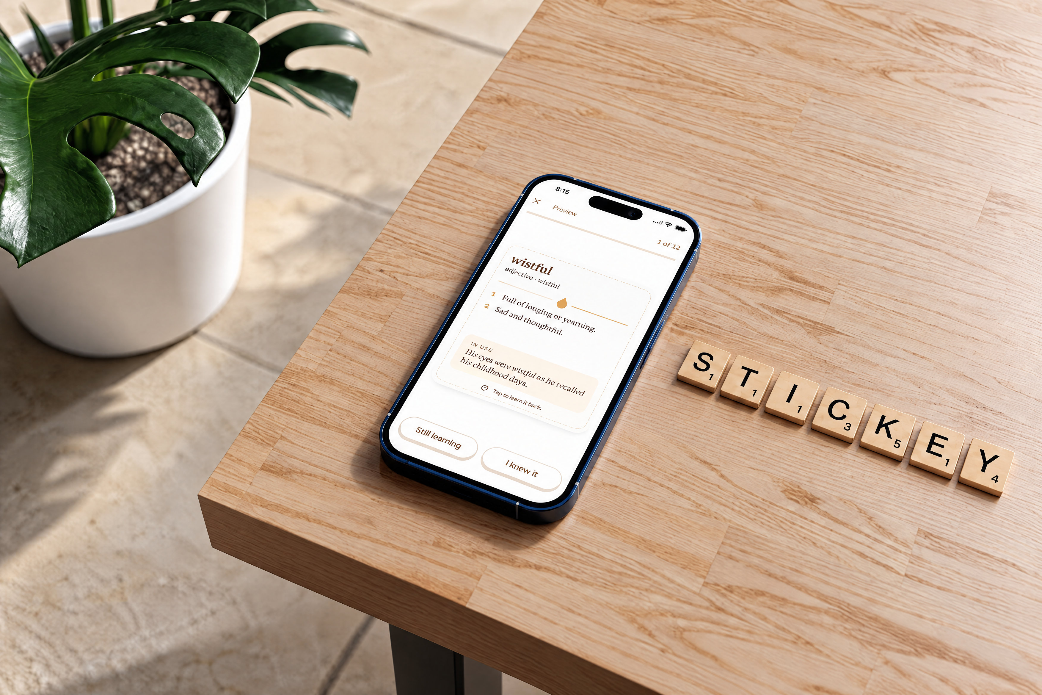 A phone showing a Stickey review card for the word wistful on a wooden table, next to letter tiles spelling STICKEY